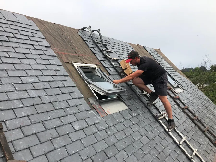 Artisan intervenant autour d'une fenêtre de toit en ardoise